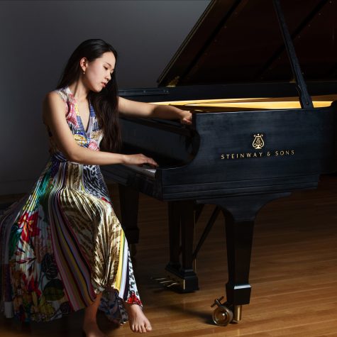 Pianist Chaeyoung Park sits at a Steinway grand piano wearing a multi-colored, pleated dress.
